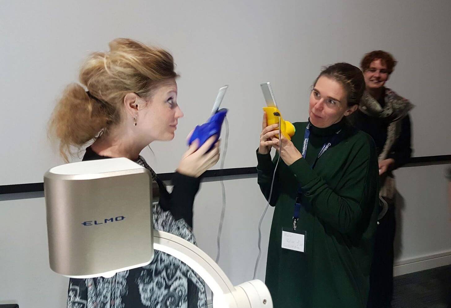 Two women test out the Kissenger device at the 2016 Love and Sex with Robots conference. 