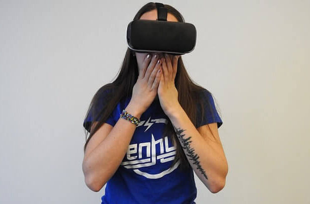A woman wearing a VR headset covering her mouth in what looks like shock.