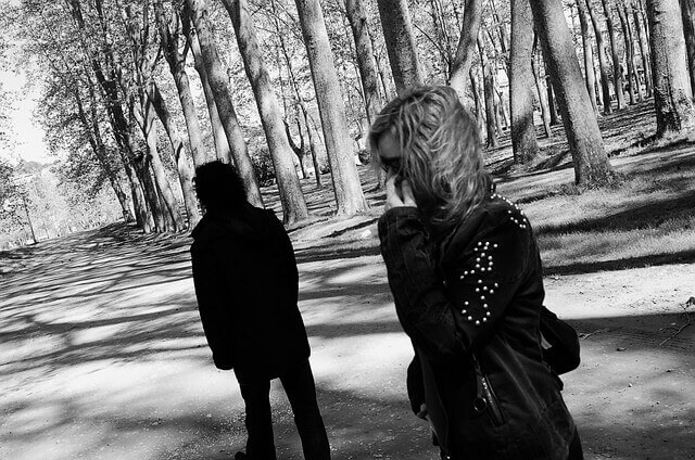 A couple appear on a forest trail looking distant from each other. 