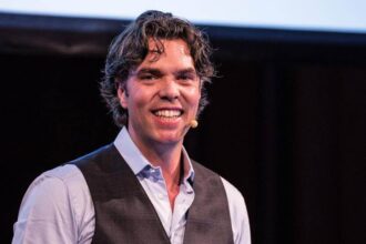 Kiiroo CEO Toon Timmermans appears on a stage wearing a face mic and a vest.