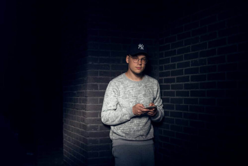 Spotlice CEO Jacob Michalak stands holding a phone before a brick wall,.