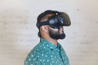 A bearded man with a green shirt wears a VR headset.