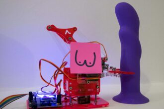 A robotic arm holds a purple dildo.