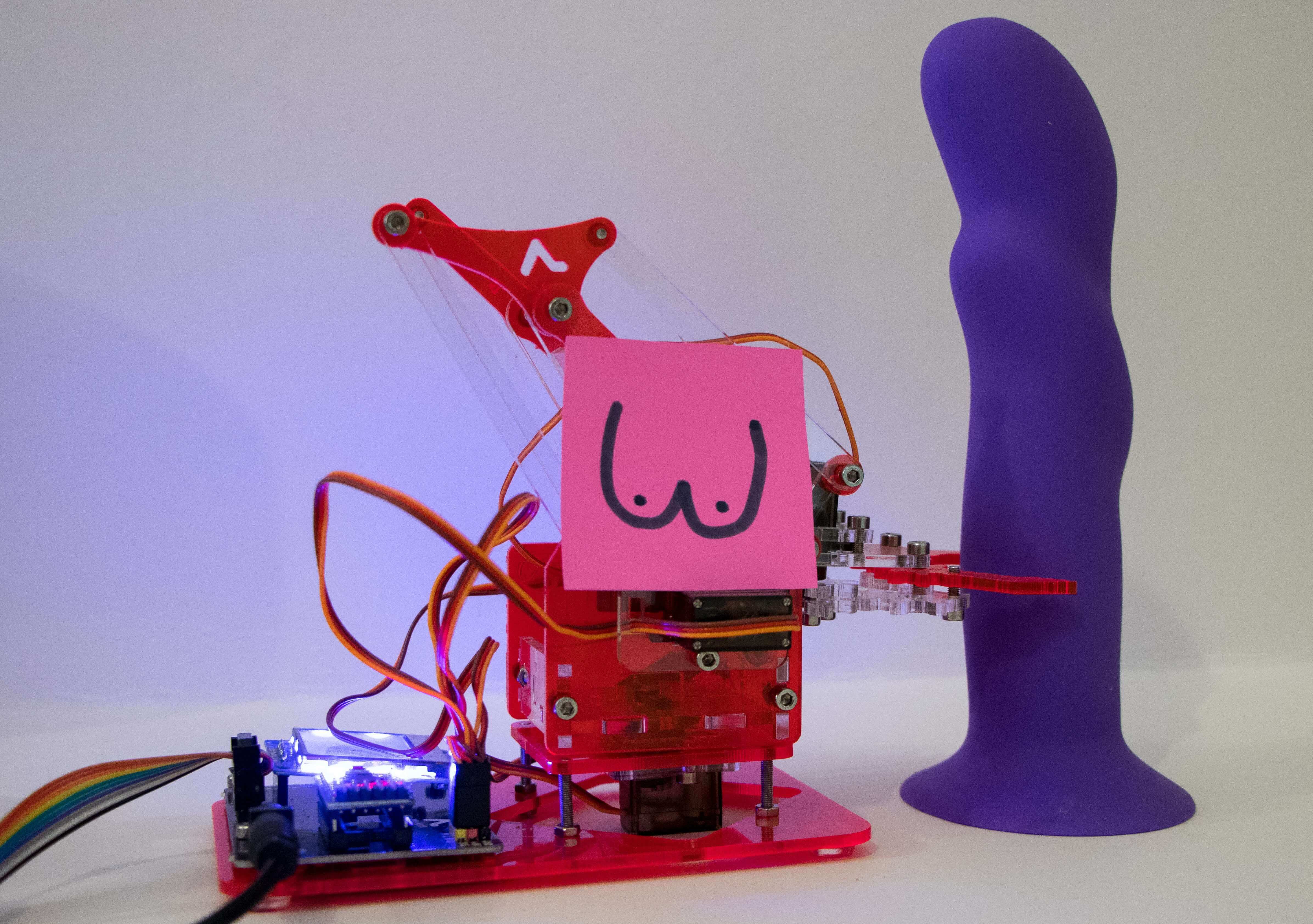 A robotic arm holds a purple dildo.
