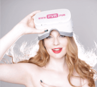 VR porn entrepreneur Ela Darling stands topless covering her breasts with one arm and holding a VR headset with the toher hand.