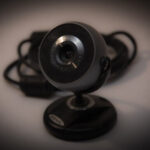 A black circular webvam on a stand appears in front of cables on a brown background.