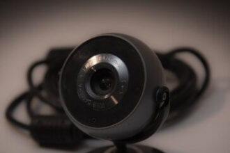 A black circular webvam on a stand appears in front of cables on a brown background.