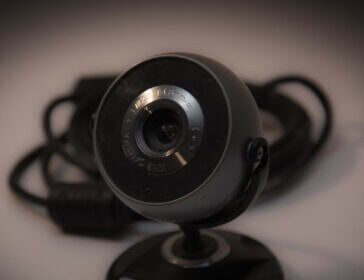 A black circular webvam on a stand appears in front of cables on a brown background.