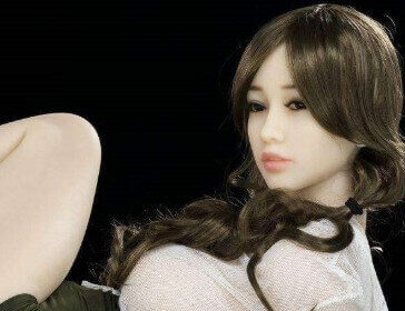 A pale skinned sex doll poses on its side in a white see-through top and short black skirt.
