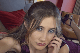 A young woman lies on her bed and looks into the camera.