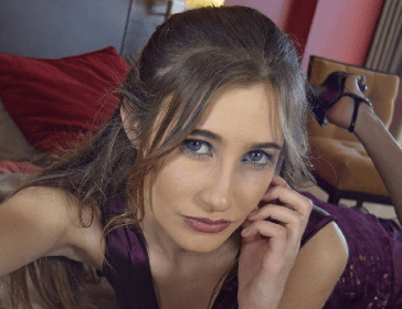 A young woman lies on her bed and looks into the camera.
