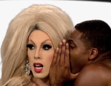 A drag queen appears shocked as a black man whispers in their ear.