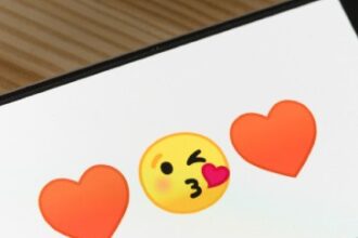 A smartphone shows two heart emojis with a yellow-face kiss emoji in the middle.