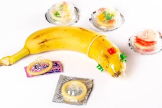 A banana is shown weraing a condom with various unopened condoms lying around it.
