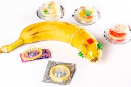 A banana is shown weraing a condom with various unopened condoms lying around it.