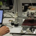 Image of a man working on laptop and 3D printer