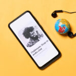 Clubhouse Invite-only Audio Chat App Open in Mobile Phone with a Globe and Earphone Display in Background
