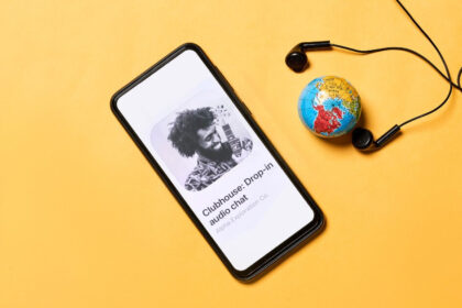 Clubhouse Invite-only Audio Chat App Open in Mobile Phone with a Globe and Earphone Display in Background