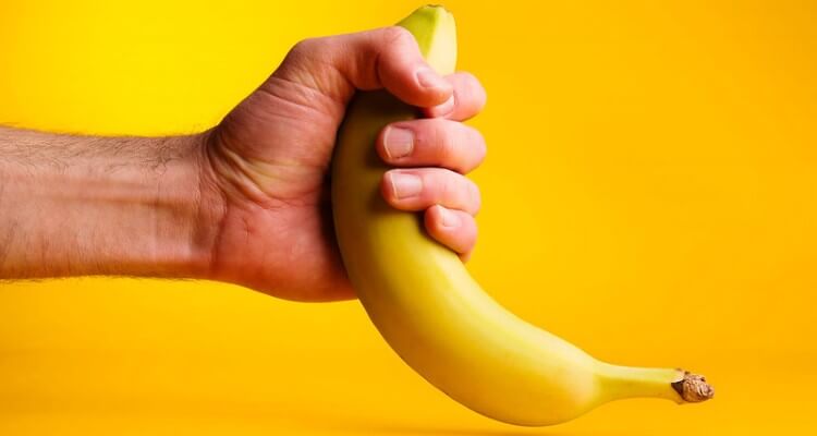 Screeshot of male hand stroking a banana to represent male handjob. Yellow background.