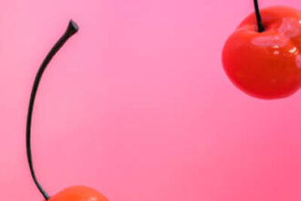 Two red cherries on a pink background.