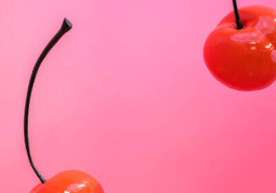 Two red cherries on a pink background.