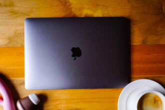 Sex toys sit next to a closed laptop and coffee on a wooden tabletop.