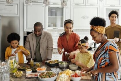 A family with four adults making dinner together with two children.
