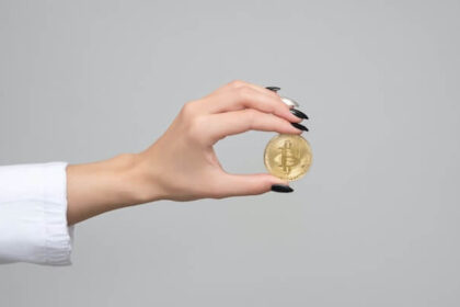 Hand with long nails holding a physical Bitcoin.
