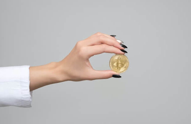 Hand with long nails holding a physical Bitcoin.