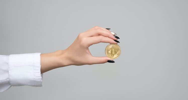 Hand with long nails holding a physical Bitcoin.