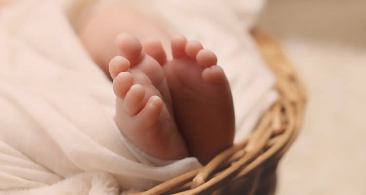Newborn baby feet poking out of a wicker basket.