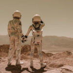 Two astronauts in space suits looking out into the distance and holding hands.