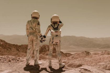 Two astronauts in space suits looking out into the distance and holding hands.
