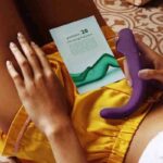 A woman lying her back holding the Crescendo 2 with a pamphlet with various positions for how to use it.