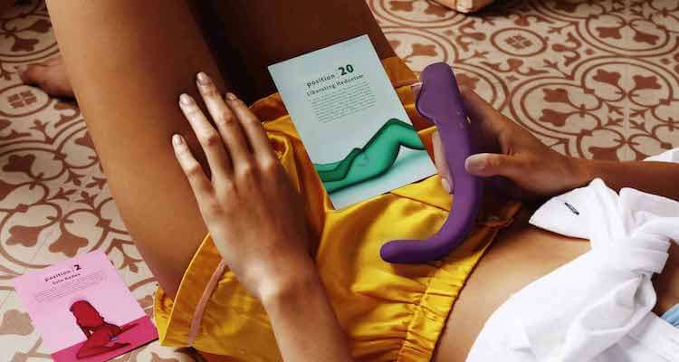 A woman lying her back holding the Crescendo 2 with a pamphlet with various positions for how to use it.