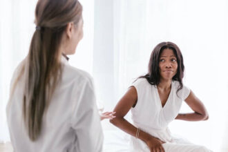 A doctor talking to a sitting patient. The patient has an uncomfortable face and holding their lower back.