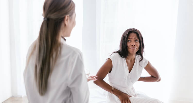 A doctor talking to a sitting patient. The patient has an uncomfortable face and holding their lower back.