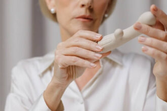 An older woman holding white vibrator, the camera focused on her hands.