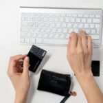 Two hands shown with one typing on a keyboard and the other holding a Visa card.