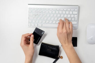 Two hands shown with one typing on a keyboard and the other holding a Visa card.