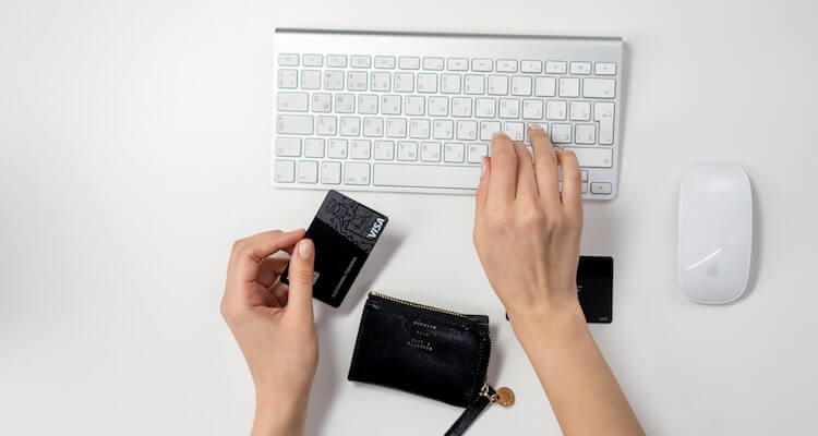 Two hands shown with one typing on a keyboard and the other holding a Visa card.